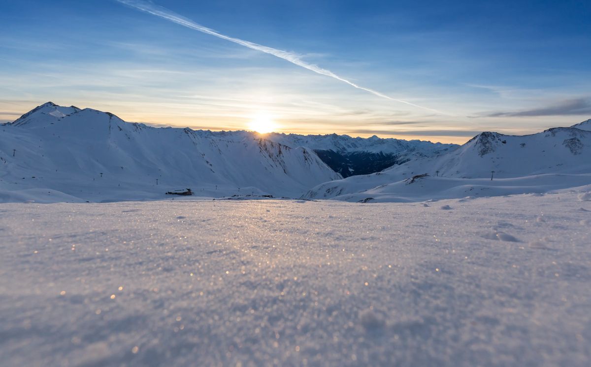 Weite Schneelandschaft in den Bergen bei Sonnenaufgang, mit sanften Hängen und glitzernder Schneeoberfläche.